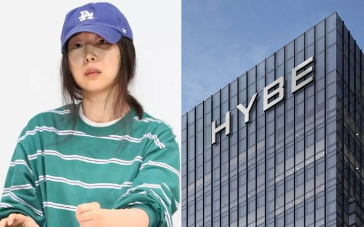 This contain an image of Min Hee Jin standing in front of a building with the hybe logo on it